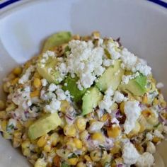 a white bowl filled with corn, avocado and feta cheese on top