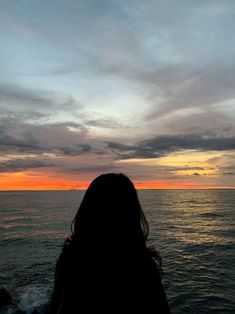 a woman standing on the edge of a cliff looking out at the ocean during sunset