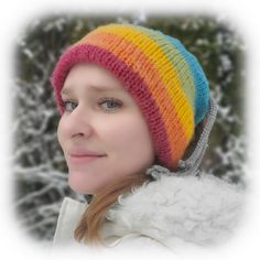 a woman wearing a multicolored knitted beanie hat in front of snow covered trees