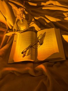 an open book with glasses on top of it sitting on a bed covered in blankets