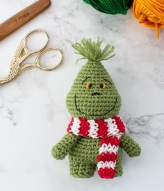 a crocheted green stuffed animal sitting next to yarn and scissors