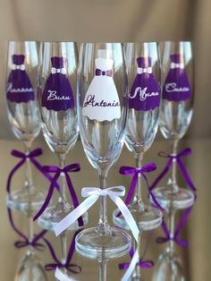 there are many wine glasses with purple ribbon around them and one has a bride's dress on it