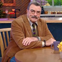 an older man sitting at a table with a cup of coffee and flowers in front of him