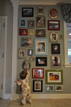 a young child standing in front of a wall with many pictures on it and holding his hand up to the ceiling