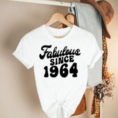 1964 Birthday Tshirt,60th Birthday Shirt,60th Birthday Gift for Women,Fabulous Since 1964 Shirt,Born In 1964 Tshirt,Hello 60 Tee,60 Year Old ---HOW TO ORDER--- 1-) Please, check and review all photos 2-) Choose your t-shirt size and color *Different styles of shirts may have different shades of same color choice due to different manufacturer brands. *For this reason, we recommend you to match shirts from the same styles if you want precisely matching colors (exa. Unisex,V-neck, Tank top, etc.). Retro White Tops For Anniversary, Retro White Top For Birthday, Vintage White Top For Birthday, Hello 60, 60th Birthday Ideas For Mom, 60th Birthday Shirt, 1964 Birthday, Moms 60th, Champagne Shirt