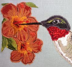 a close up of a bird with flowers on it's back side and an orange flower in the background