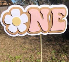 a cake topper with the word one written in pink and white flowers on it