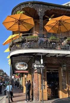 people are standing outside an outdoor cafe with yellow umbrellas on the balcony and tables