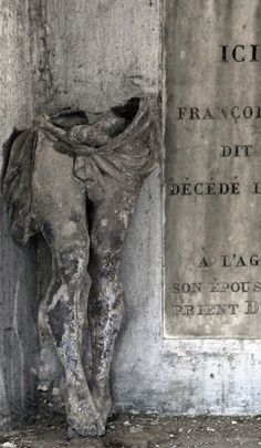 an old statue next to a plaque on the side of a building with writing on it