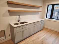 an empty kitchen with white counter tops and wooden shelves on the wall, along with hardwood flooring