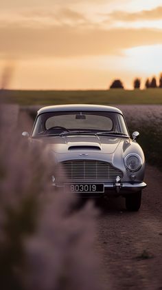 an old car is parked on the side of a dirt road near some grass and trees