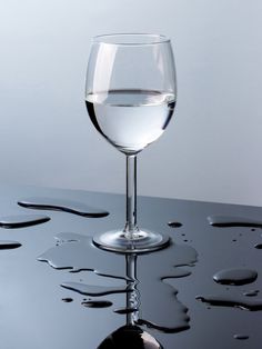 a glass of water sitting on top of a black table with drops of water around it