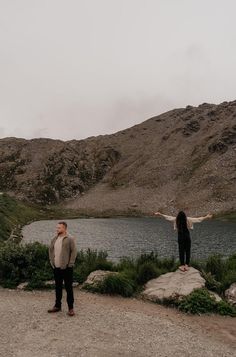 two people standing on rocks near a body of water