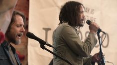 two people singing into microphones in front of a banner