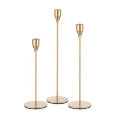 three gold candlesticks on white background with one candle in the middle and one standing upright