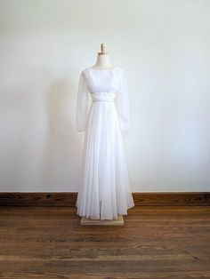 a white dress on a mannequin stand in front of a wall and wooden floor