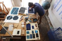 a man sitting at a wooden table working on some art work with paint and brushes