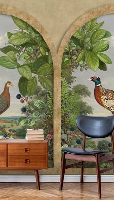 two birds sitting on top of a wooden table in front of a wall with paintings