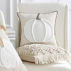 a white chair with two pillows and a pumpkin pillow on top of it, sitting in front of a window