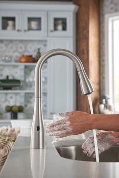 a person washing their hands under a kitchen faucet