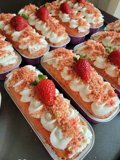 there are many desserts in the trays with strawberries on top and white frosting