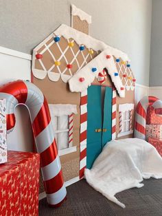 Cardboard gingerbread house mounted on a wall as decor at a Christmas party. Gingerbread Bash Church, Christmas Backdrop Ideas For School, Christmas Diy Gingerbread House, Gingerbread House Life Size Diy, How To Make A Gingerbread House Out Of Cardboard, Candy Cane Photo Booth, Diy Gingerbread Backdrop, Ginger Bread House Christmas Decor