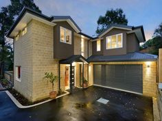 a two story house with lights on in the front yard and driveway at night time