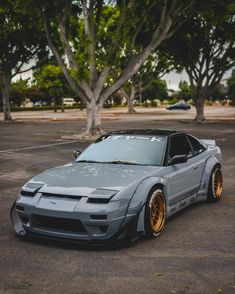 a gray car parked in a parking lot next to some trees and cars with gold rims