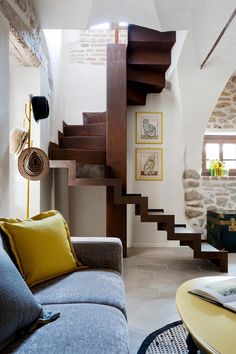 a living room filled with furniture next to a stone wall and wooden staircase leading up to the second floor