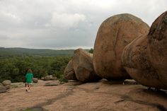 two large rocks sitting on top of a rock covered hillside with trees in the background