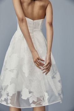 the back of a woman's white dress with flowers on it and her hands in her hair