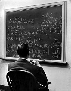 a man is sitting in front of a blackboard with many calculations on it and writing on it