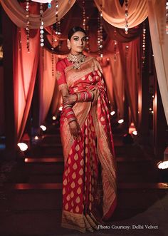 a woman in a red and gold sari standing under an archway with lights on either side