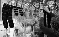 a woman looking at socks hanging on a clothes line in front of a tree and building