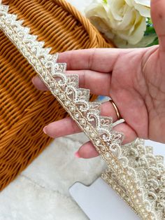 a hand holding a tiara in front of a wicker basket and white flowers