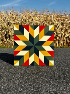 a small square shaped piece of art sitting in front of a corn field