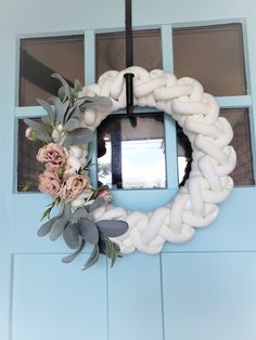 a white wreath with flowers and leaves hanging on a blue door