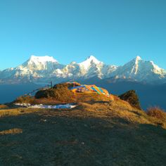 there is a tent on top of a hill with mountains in the background and blue sky