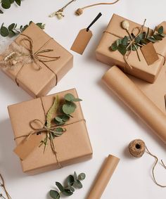 three wrapped presents with greenery and twine tied to them on a white surface