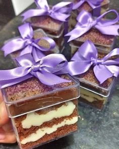 there are several desserts with purple ribbons in the box on the table and someone holding one