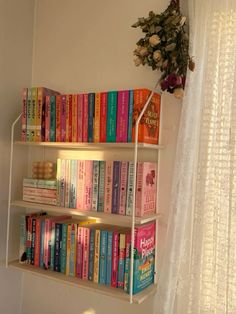 a white book shelf filled with lots of books next to a window covered in sheer curtains