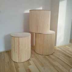 three round wooden stools sitting on top of a hard wood floor next to a white wall