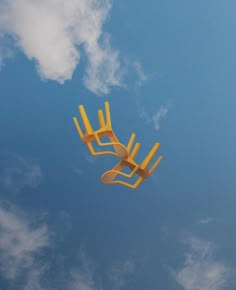 a kite flying high in the blue sky with clouds behind it and two chairs on each side