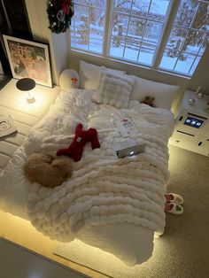 a teddy bear is laying on a bed with white blankets and pillows in front of the window