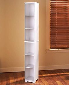 a tall white book shelf sitting in the corner of a room next to a window