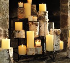 many candles are lit in front of a stone fireplace with logs stacked on the mantle