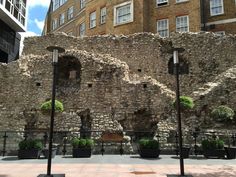 an old stone wall with potted plants in front of it on a city street