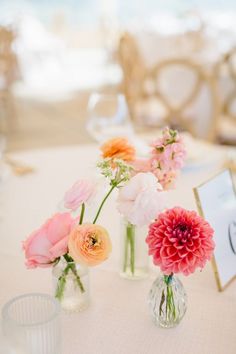 three vases filled with flowers sitting on top of a white tablecloth covered table