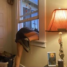 a woman bending over in front of a window with a lamp next to her on the floor