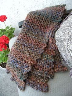 a crocheted scarf sitting on top of a pillow next to a potted plant